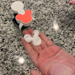 May include: A white soap dispenser with a red Mickey Mouse head on the top. The dispenser is dispensing white foam into a hand.