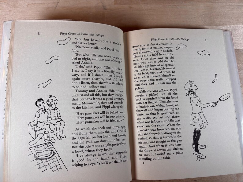 Puede incluir: Un libro abierto con ilustraciones en blanco y negro. Una p&aacute;gina muestra a dos ni&ntilde;os y panqueques, la otra a una ni&ntilde;a volteando un panqueque. El texto es visible en ambas p&aacute;ginas, que describe una historia.