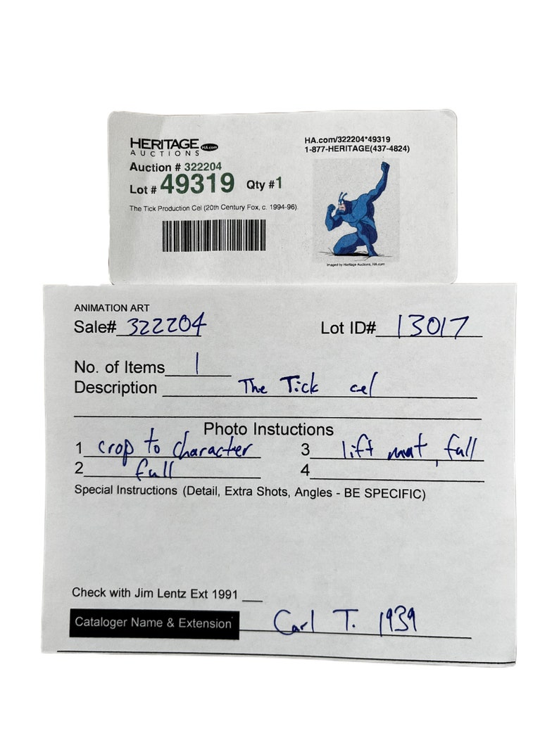 May include: A close-up of a white card with black text. The card is titled "Animation Art" and includes the text "Sale# 322204", "Lot ID# 13017", "No. of Items 1", "Description The Tick cel", "Photo Instructions 1 crop to character 2 full 3 lift naat, full 4", "Special Instructions (Detail, Extra Shots, Angles - BE SPECIFIC)", "Check with Jim Lentz Ext 1991", "Cataloger Name & Extension Carl T. 1939".