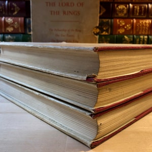 May include: A set of three vintage hardcover books with white covers and red spines. The top book has the title "The Lord of the Rings" printed on the spine.