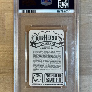 May include: A white card with a picture of Muhammad Ali, a famous boxer, and text about his life and career. The card is from the "Our Heroes" series of trading cards. The card is in a protective plastic case.