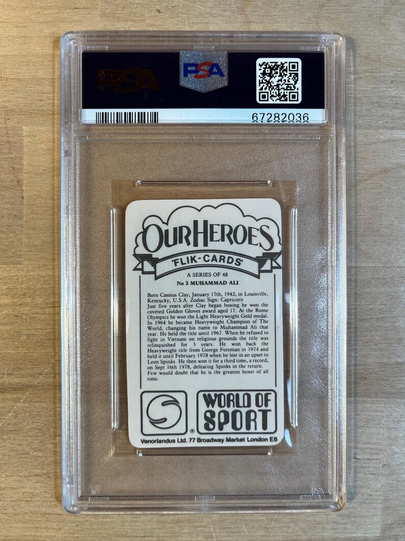 May include: A white card with a picture of Muhammad Ali, a famous boxer, and text about his life and career. The card is from the "Our Heroes" series of trading cards. The card is in a protective plastic case.