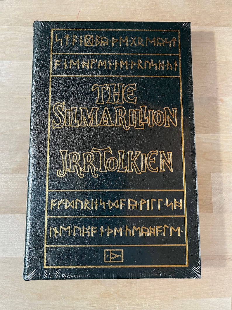 May include: A dark green hardcover book with gold lettering. The title is "The Silmarillion" by J.R.R. Tolkien. The cover features a decorative design of gold symbols.