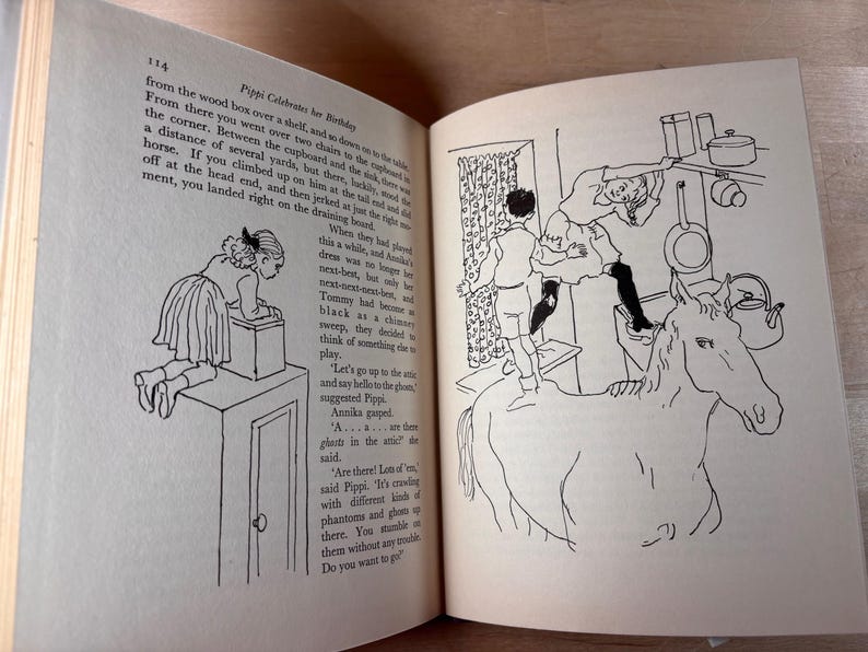 Puede incluir: Un libro abierto con ilustraciones en blanco y negro. Una p&aacute;gina muestra a una ni&ntilde;a sobre una caja, la otra representa a una ni&ntilde;a sobre un caballo alcanzando objetos en una cocina. El texto es visible.
