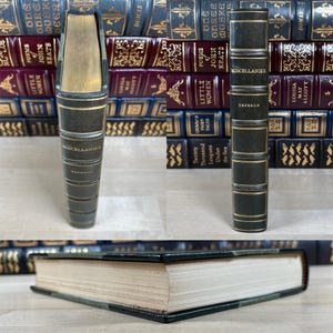 May include: A vintage book titled "Miscellanies" by Emerson. The book has a dark green cover with gold accents and text. The spine displays the title and author's name. The book is part of a collection of antique books with various colors and titles.