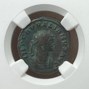Könnte beinhalten: Eine römische Bronzemünze mit dem Porträt eines Herrschers, der eine Krone trägt, und der Inschrift "IMP C LVD DOMITIANVS AVG GERM".