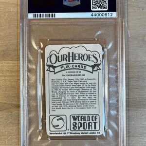 May include: A vintage trading card featuring a black and white photo of Muhammad Ali, a famous boxer. The card has a white background with black text that reads "Our Heroes" and "Flik-Cards". The text also includes Ali's birth name, Cassius Clay, and his birthdate. The card is in a protective plastic case.
