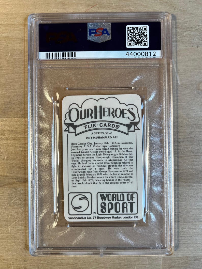 May include: A vintage trading card featuring a black and white photo of Muhammad Ali, a famous boxer. The card has a white background with black text that reads "Our Heroes" and "Flik-Cards". The text also includes Ali's birth name, Cassius Clay, and his birthdate. The card is in a protective plastic case.