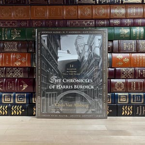 May include: A book cover with a black and white illustration of a city with a large ship in the background. The title of the book is "The Chronicles of Harris Burdick" by Chris Van Allsburg. The book cover is surrounded by a collection of books.