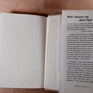 May include: An open hardcover book with a white interior page and a dust jacket flap featuring black printed text titled What reviewers say about Pippi, including quotes from Virginia Kirkus, Horn Book, and the New York Herald Tribune.