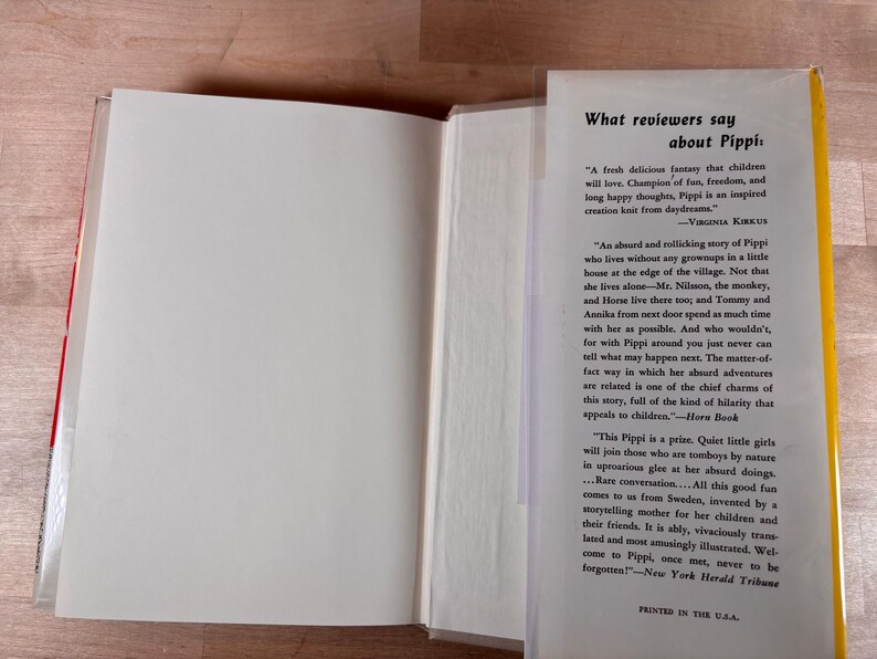 May include: An open hardcover book with a white interior page and a dust jacket flap featuring black printed text titled What reviewers say about Pippi, including quotes from Virginia Kirkus, Horn Book, and the New York Herald Tribune.