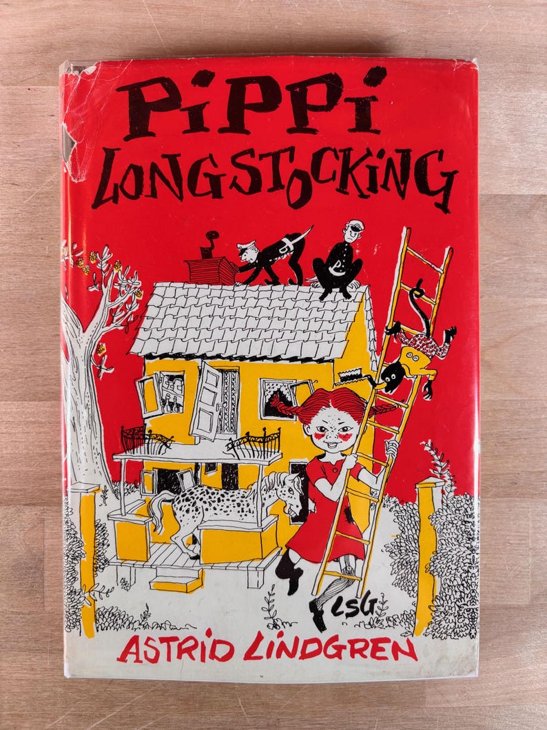 May include: A hardcover book titled Pippi Longstocking by Astrid Lindgren with a bright red cover. The illustration features a yellow house, a spotted horse on a porch, a monkey on a ladder, and a girl with red braids in a red dress.