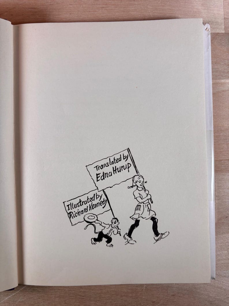 May include: A book page featuring a black ink line drawing of a person and a small creature walking together. The person carries a sign reading Translated by Edna Hurup, while the creature carries a sign reading Illustrated by Richard Kennedy.