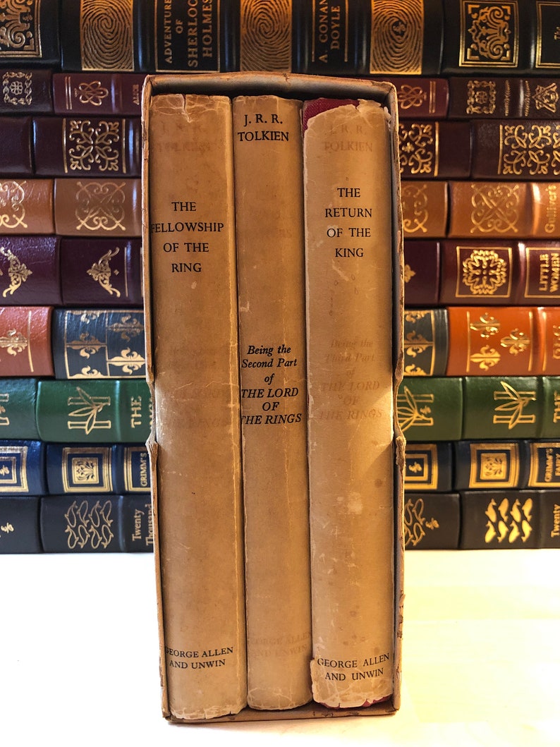 May include: A set of three vintage hardcover books, The Fellowship of the Ring, The Two Towers, and The Return of the King, by J.R.R. Tolkien. The books are bound in brown paper with gold lettering and are part of a larger collection of books.