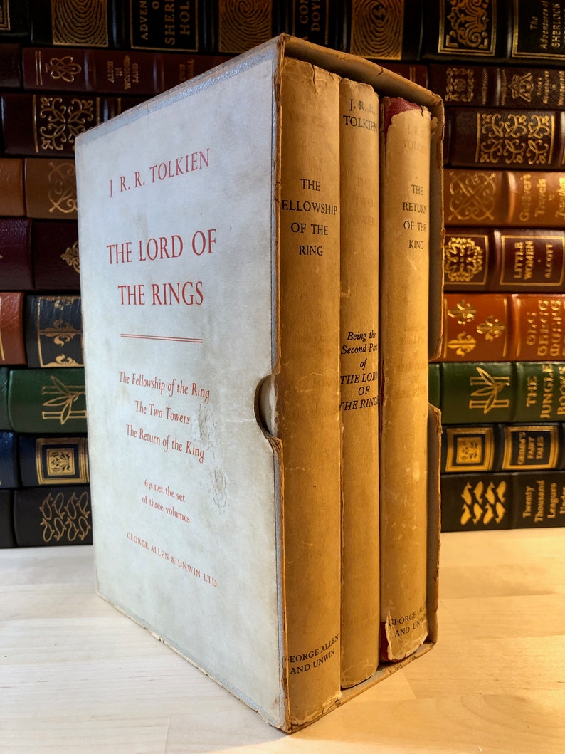 May include: A three-volume set of The Lord of the Rings by J.R.R. Tolkien. The books are bound in brown cloth with gold lettering. The set is in a slipcase with a white background and red lettering.