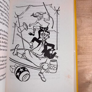 May include: A black and white book illustration depicting a circus scene with a girl jumping over a ringmaster. The ringmaster holds a cane and wears a coat, while the girl has braided hair. Two barrels decorated with stars are on the ground.
