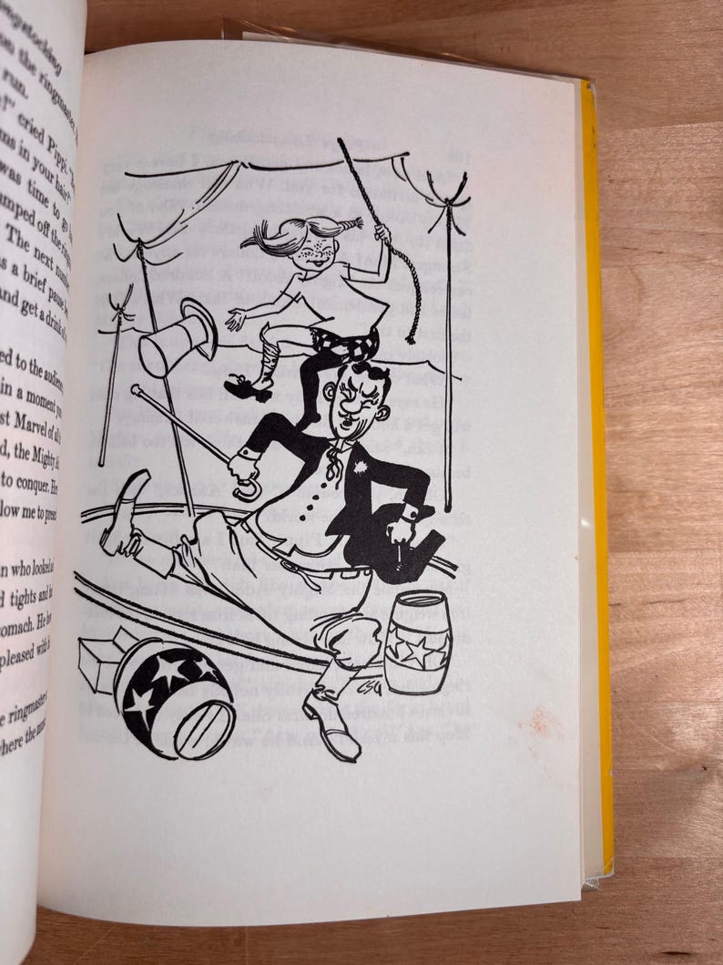 May include: A black and white book illustration depicting a circus scene with a girl jumping over a ringmaster. The ringmaster holds a cane and wears a coat, while the girl has braided hair. Two barrels decorated with stars are on the ground.