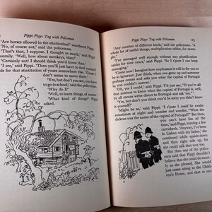 May include: An open book titled Pippi Plays Tag with Policemen, featuring two pages of printed text and black and white line illustrations. The left page shows a house under a tree, and the right page depicts two policemen standing by a fence.