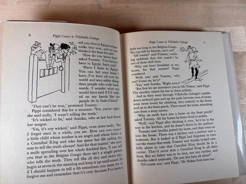 Puede incluir: Un libro abierto con ilustraciones y texto. Las p&aacute;ginas muestran dibujos en blanco y negro de personajes y texto de la historia "Pippi Comes to Villekulla Cottage". El libro est&aacute; abierto sobre una superficie de madera.