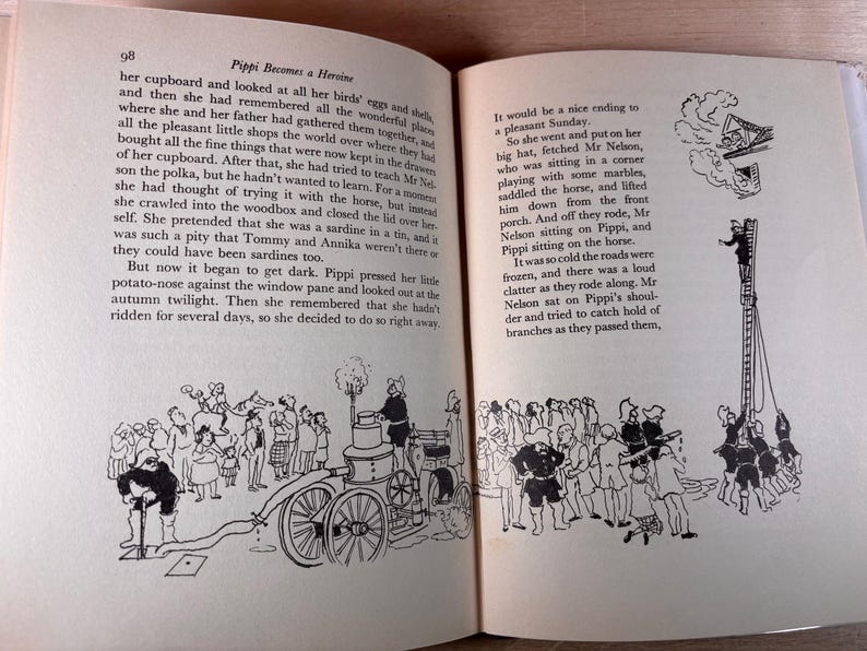 May include: An open book page 98 titled Pippi Becomes a Heroine with black and white illustrations. The text describes Pippi Longstocking's adventures. Below the text, drawings show a vintage fire engine with a hose and a group of people near a tall ladder.