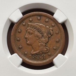 May include: A copper-colored coin from 1853, featuring a profile of a woman with the word "LIBERTY" above her head. The coin is surrounded by stars and is encased in a protective holder.