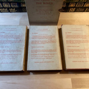 May include: Three vintage paperback books with red and white text on a white background. The books are titled "The Hobbit" by J.R.R. Tolkien. The books are published by George Allen and Unwin Ltd.