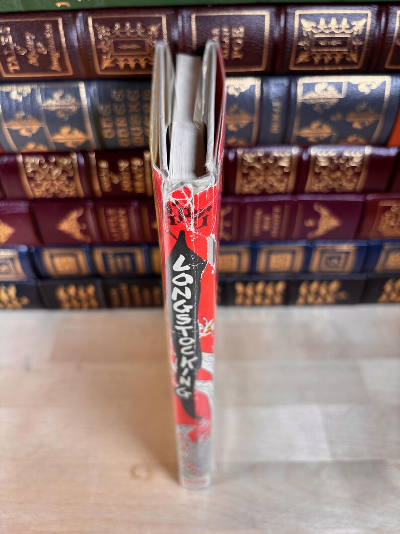May include: A book spine featuring a red background with white text that reads Pippi Longstocking. The spine shows signs of wear, including frayed edges and peeling paper at the top. The book is positioned vertically, displaying its narrow side.