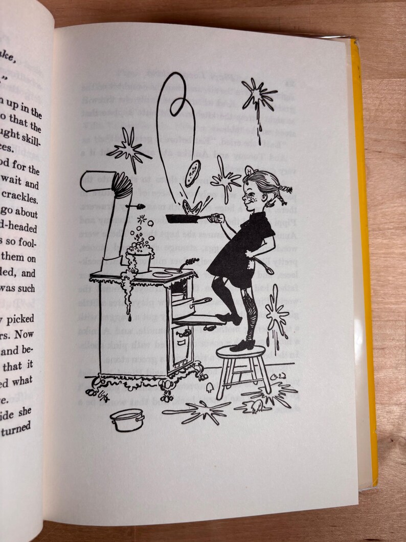 May include: A black and white line drawing illustration on a book page depicting a person standing on a small stool, cooking at a stove. The person holds a frying pan with a pancake flipping in the air, while bubbles and splashes surround the scene.