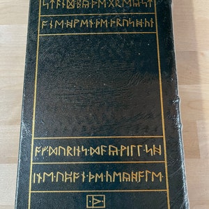 May include: A black leather-bound book with gold lettering on the spine and front cover. The lettering is in a runic alphabet. The book is closed and appears to be quite old.