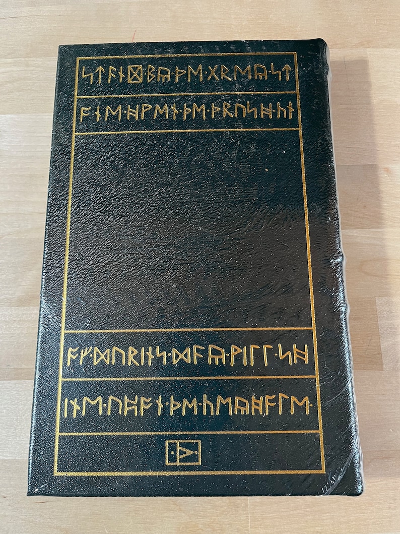 May include: A black leather-bound book with gold lettering on the spine and front cover. The lettering is in a runic alphabet. The book is closed and appears to be quite old.