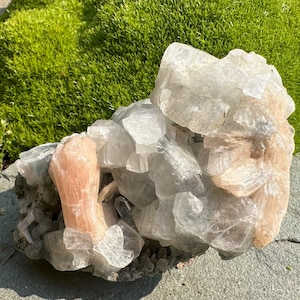 Op de afbeelding: Een cluster van heldere en roze selenietkristallen. De kristallen zijn in een natuurlijke formatie gerangschikt, waarbij sommige kristallen op elkaar lijken te zijn gestapeld. De kristallen zijn doorschijnend en hebben een lichte glans.