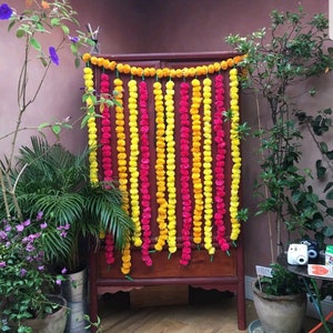 May include: A wooden cabinet decorated with yellow and pink flower garlands. The garlands are made of marigold and carnation flowers.