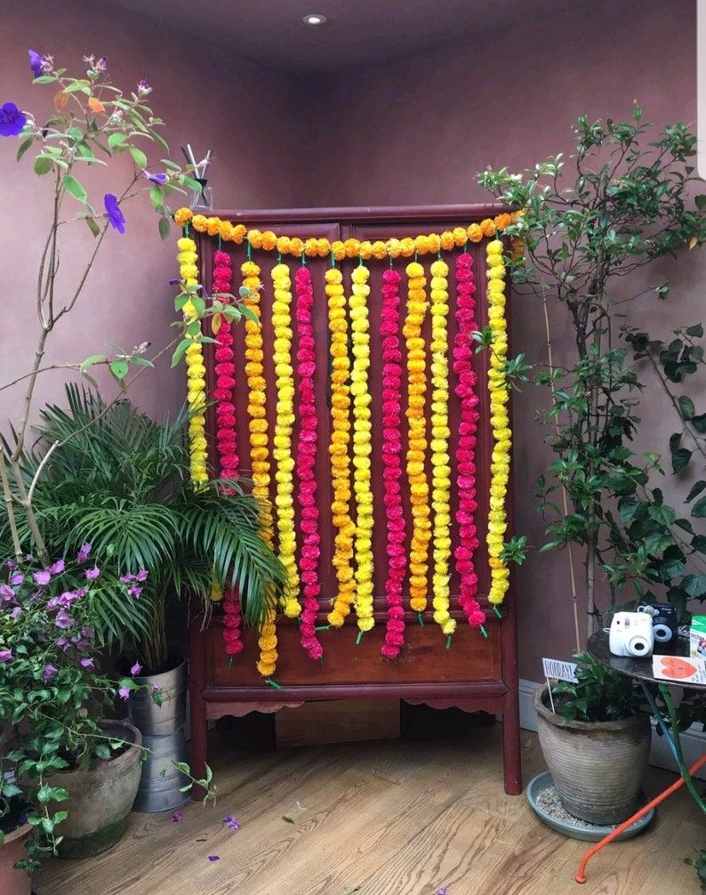 May include: A wooden cabinet decorated with yellow and pink flower garlands. The garlands are made of marigold and carnation flowers.