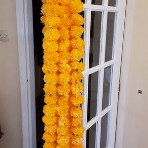 May include: A long garland of yellow marigold flowers, strung together and hanging from a white door.