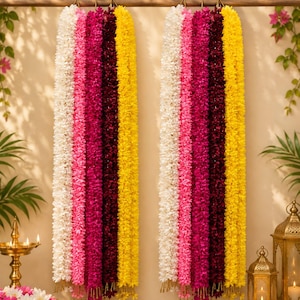 May include: Two sets of vertical floral garlands hanging from a horizontal rod. Each garland features four distinct colour sections: white, bright pink, deep maroon, and yellow. The flowers are densely packed, creating a long, textured appearance.