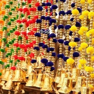May include: A colorful garland of pom-poms and bells. The garland is made of gold beads and has pom-poms in shades of pink, orange, yellow, green, red, and blue. The bells are gold and are attached to the garland at regular intervals.