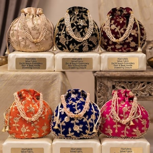 Peut inclure: Six pochettes rondes à cordon en velours beige, noir, bordeaux, orange, bleu et rose. Chacune présente une broderie dorée zari et à paillettes, une anse en perles et une fermeture à cordon. Chaque pochette repose sur un socle avec étiquette.