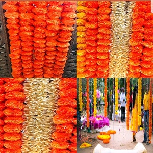 May include: Orange and cream paper flower garlands hanging from a ceiling and strung across a pathway. The garlands are made of paper flowers that resemble marigolds.