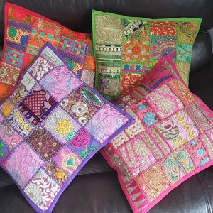 Könnte beinhalten: Vier dekorative Kissen mit Patchwork-Muster. Die Kissen bestehen aus verschiedenen Stoffen und Farben, darunter Pink, Lila, Grün und Rot. Die Kissen sind mit Pailletten und Stickereien verziert.
