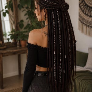 May include: Long dark brown synthetic dreadlocks styled in a half-up bun. The dreadlocks feature decorative white thread wrapping in a crisscross pattern and small silver-toned metal beads throughout the length of the hair extensions.