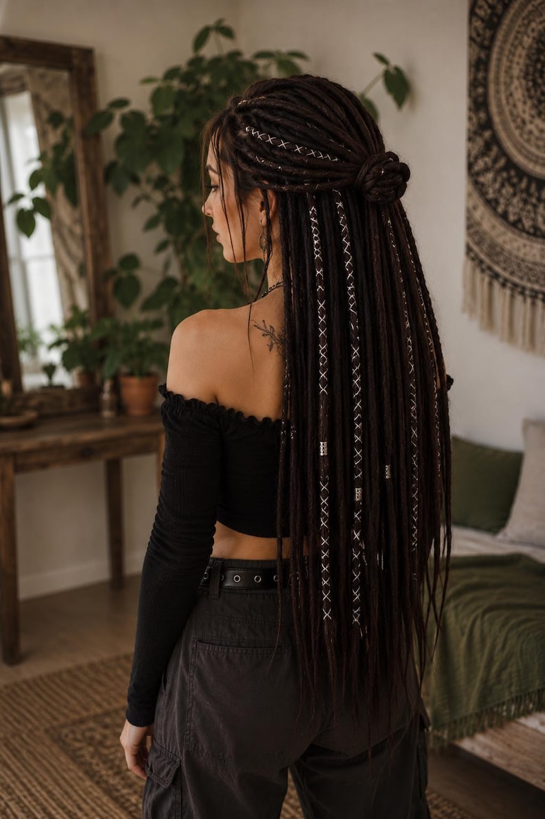 May include: Long dark brown synthetic dreadlocks styled in a half-up bun. The dreadlocks feature decorative white thread wrapping in a crisscross pattern and small silver-toned metal beads throughout the length of the hair extensions.