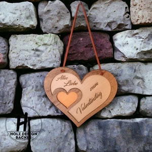 Pode incluir: Um letreiro de madeira em forma de coração com o texto "Alles Liebe zum Valentinstag" (Todo o amor para o Dia dos Namorados) em alemão. O letreiro está pendurado em uma parede de pedra.