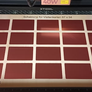 Puede incluir: Una plantilla blanca con el texto "Schablone für Visitenkarten 87 x 54" y "Anlegen bei 0,6" impreso en ella. La plantilla tiene 12 recortes rectangulares para tarjetas de visita.