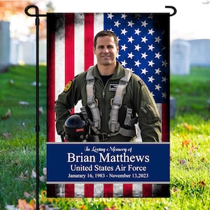 May include: A memorial garden flag with a faded American flag background and a photo of a man in a military uniform. The text reads "In Loving Memory of Brian Matthews United States Air Force January 16, 1983 - November 13, 2023".
