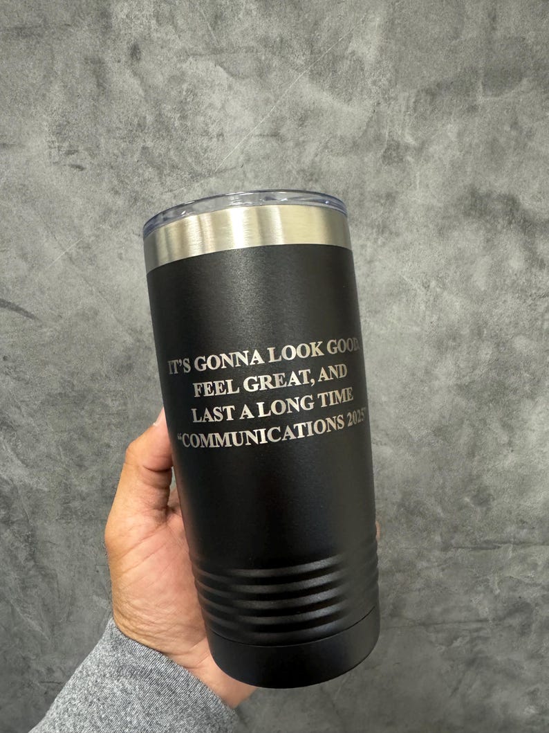 May include: Black insulated tumbler with a silver rim and lid. The tumbler has the text "IT'S GONNA LOOK GOOD FEEL GREAT, AND LAST A LONG TIME COMMUNICATIONS 2025" in white. The tumbler is cylindrical and appears to be made of stainless steel.