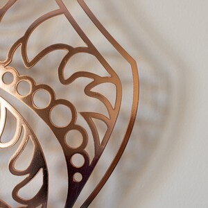 May include: A copper-colored metal cutout with a decorative, intricate design. The cutout features a repeating pattern of circles, swirls, and leaves.