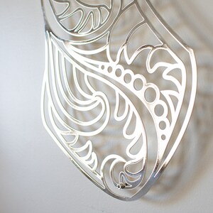 May include: Silver metal wall decor with a cut-out design of swirling leaves and flowers.