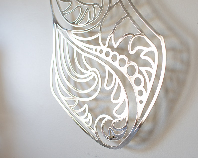 May include: Silver metal wall decor with a cut-out design of swirling leaves and flowers.