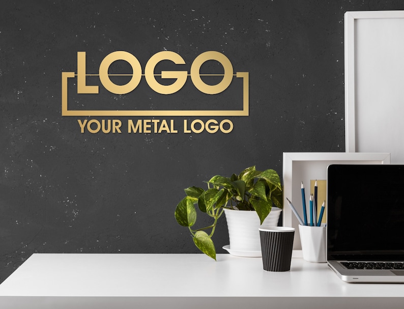 May include: A gold metal logo sign with the word "LOGO" in a bold font. The sign is mounted on a black wall with a white frame around it. The text "YOUR METAL LOGO" is below the logo.