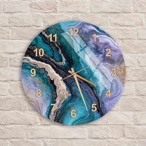May include: A round wall clock featuring a swirling marble-like pattern in shades of teal, deep blue, purple, and white with gold accents. The clock face displays gold-coloured numbers from 1 to 12 and thin gold hands for the hour, minute, and second.